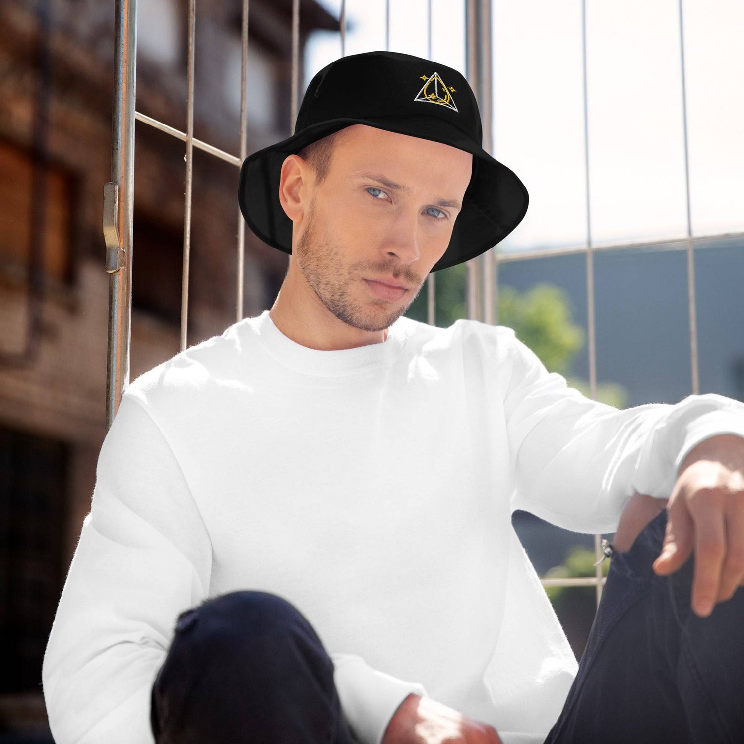 Man sitting outdoors in a white sweatshirt and black bucket hat featuring a prism and star design, perfect for sun protection and style.