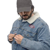 Light blue denim sherpa jacket with sustainable wool lining, showcasing a red embroidered chest logo. Modeled with button closure.